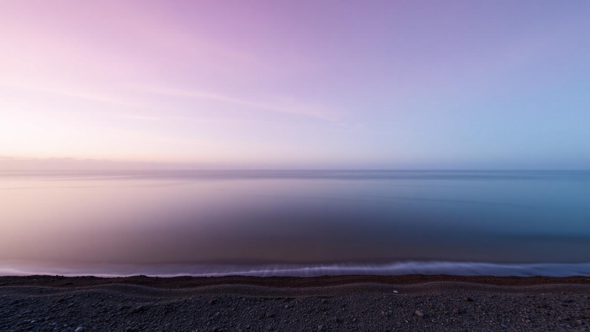 Calm shoreline at dawn under a soft pastel sky